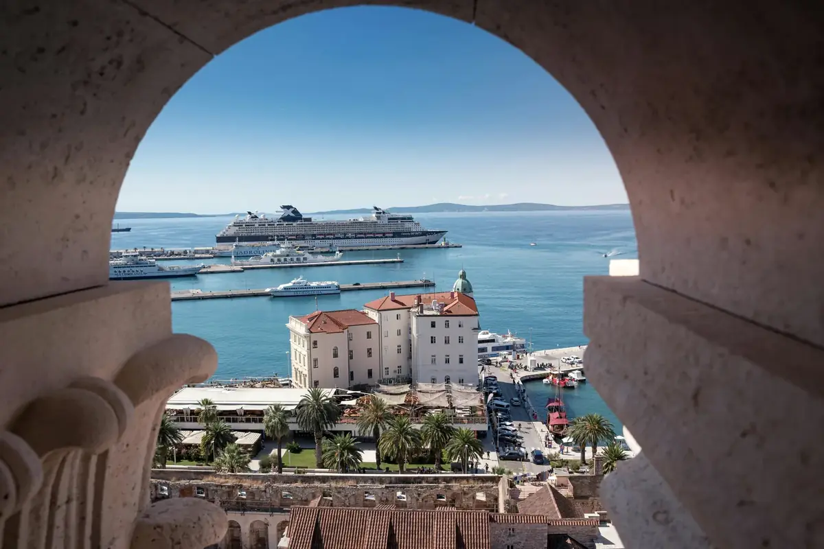 View through a stone archway towards Split's harbour, a ferry and the islands